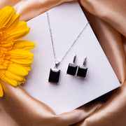 A black stone pendant set with a necklace and earrings, displayed on a white card with a yellow flower on the side.